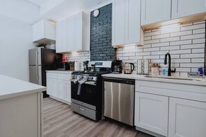 A modern kitchen with white cabinets, a black stove, stainless steel appliances, and a brick accent wall.