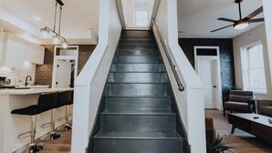 Eine Treppe führt zu einer zweiten Etage, einem Küchenbereich mit Barhocker und einer Sitzecke mit Sofa und Couchtisch.