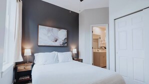 Ein Schlafzimmer mit einem Bett, Nachttischen, einem Gemälde und einer Tür zu einem Badezimmer.