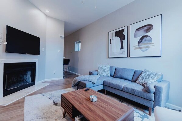 A modern living room with a flat-screen TV, a fireplace, a sectional sofa, and two framed artworks on the wall.