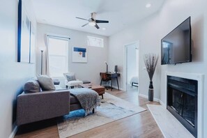 A modern living room with a sofa, a fireplace, a TV, and a ceiling fan.