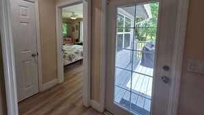 A hallway leading to a bedroom with a bed and a window overlooking a deck.