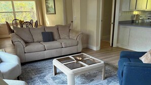 A living room with a beige sofa, a blue sofa, a coffee table, and a dining area with chairs and a table.