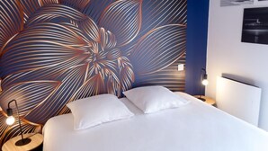 A modern hotel room with a large floral-patterned headboard, a neatly made bed with white linens, and a bedside table with a lamp.