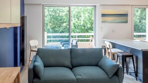 A modern living room with a grey sofa, a wooden table, and a kitchen area with a bar counter.