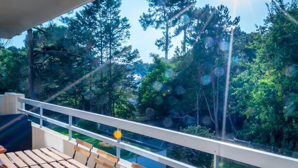 A wooden deck with a white railing overlooking a forested area.