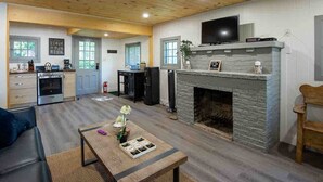 Un amplio salón con chimenea, un televisor montado encima y una cocina al fondo.