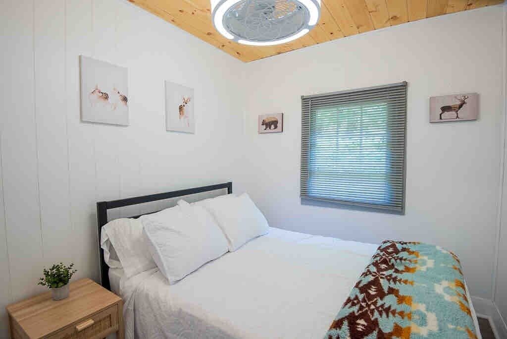 Une chambre à coucher avec un lit, une table de chevet ornée d’une plante et des œuvres d’art accrochées au mur.