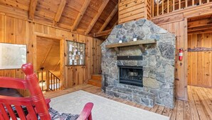 Un interior de madera con chimenea de piedra, paredes de madera y una silla roja.