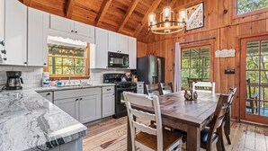 Una cabaña de madera con cocina que cuenta con gabinetes blancos, una encimera de mármol y un comedor con mesa y sillas de madera.