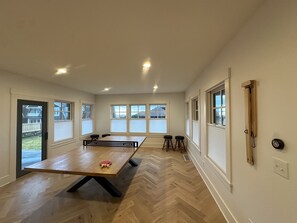 A spacious room with a large wooden table, two stools, and a ping pong table.