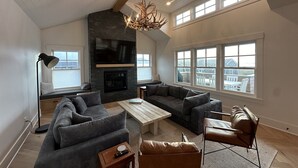 A spacious living room with a fireplace, large windows, and a high ceiling. - The Ridge - Gearhart, OR (Gearhart)