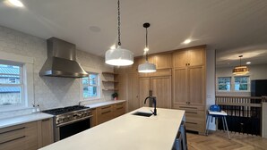 A modern kitchen with a large island, wooden cabinets, and pendant lighting. - The Ridge - Gearhart, OR (Gearhart)