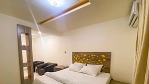 Une chambre d’hôtel avec un lit, une table de chevet, une chaise et une tête de lit en bois.