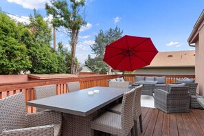 Eine Terrassengruppe im Freien mit Esstisch, Korbmöbeln und einem roten Sonnenschirm.