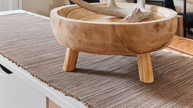 Una stanza con una grande finestra, un tavolo di legno con una ciotola e cuscini bianchi e neri.