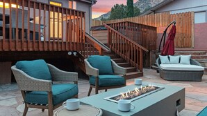 Un'area patio con mobili in vimini, un braciere e una scala che conduce a un ponte superiore.