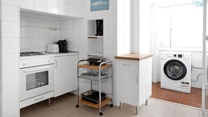 Una cocina compacta con armarios blancos, estufa, cafetera, carrito y lavadora.