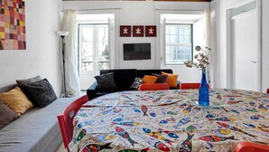 Una habitación acogedora con una mesa redonda, un sofá y una cama. Hay ventanas, un ventilador de techo y obras de arte en las paredes.