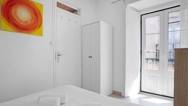 Un dormitorio con cama, toallas blancas, armario y puerta corrediza de vidrio a un balcón.
