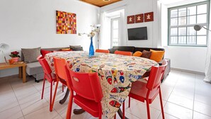 Un comedor con una mesa redonda cubierta con un mantel colorido, rodeado de sillas rojas.