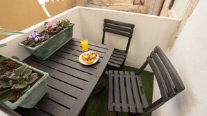 Un pequeño espacio al aire libre con mesa y sillas, una planta en maceta y un vaso de zumo de naranja.