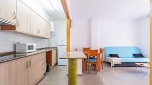Eine kleine Küche mit Mikrowelle, Kühlschrank und Holzschränken. Es gibt einen Essbereich mit Tisch und Stühlen sowie ein blaues Sofa im Wohnbereich.