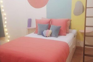 A bedroom with a bed, pillows, a bedside table, and a wall-mounted shelf.