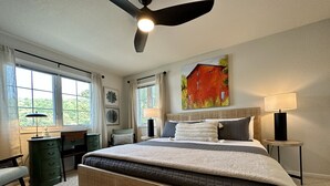 Quarto com cama grande, escrivaninha, cadeira, abajur e ventoinha de teto.