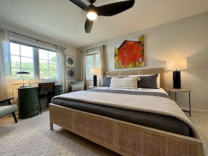 A bedroom with a large bed, a desk, a chair, a standing lamp, and a ceiling fan.