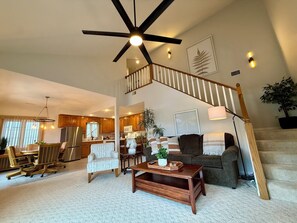 A spacious living area with a high ceiling, a wooden staircase, a dining area, and a kitchen. - The Stillwater Retreat (Camdenton)