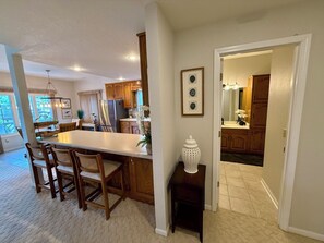 A spacious kitchen with wooden cabinets, a large island with bar stools, and a view of the backyard through the open door. - The Stillwater Retreat (Camdenton)