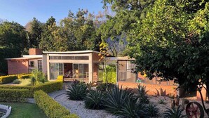 Une maison moderne dotée d’une véranda en verre, entourée de jardins bien entretenus et bordée d’un chemin de gravier.
