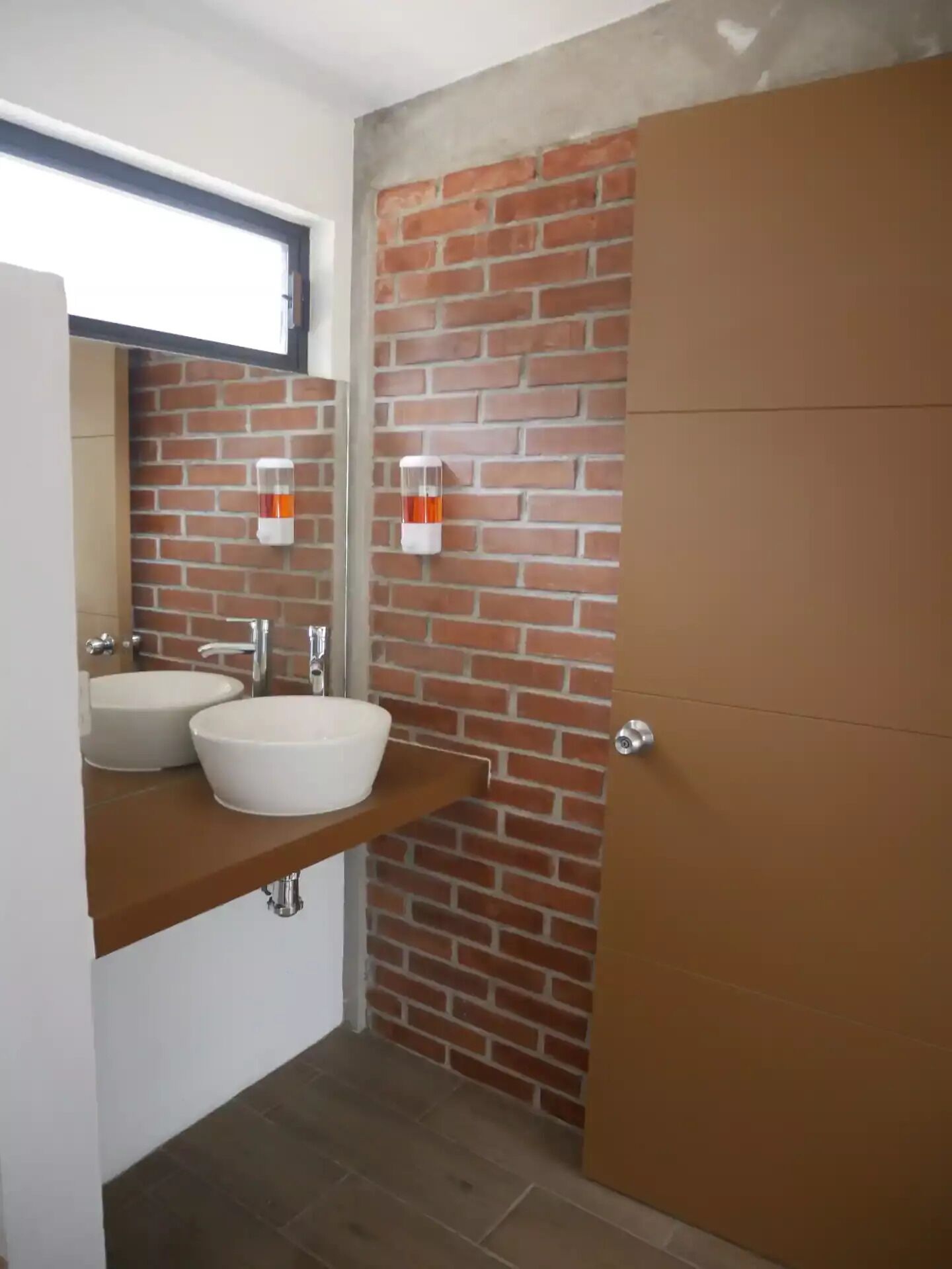 Un bagno con parete in mattoni, due lavabi bianchi e un mobile contenitore in legno.