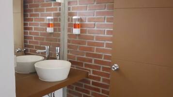 Un bagno con parete in mattoni, due lavabi bianchi e un mobile contenitore in legno.