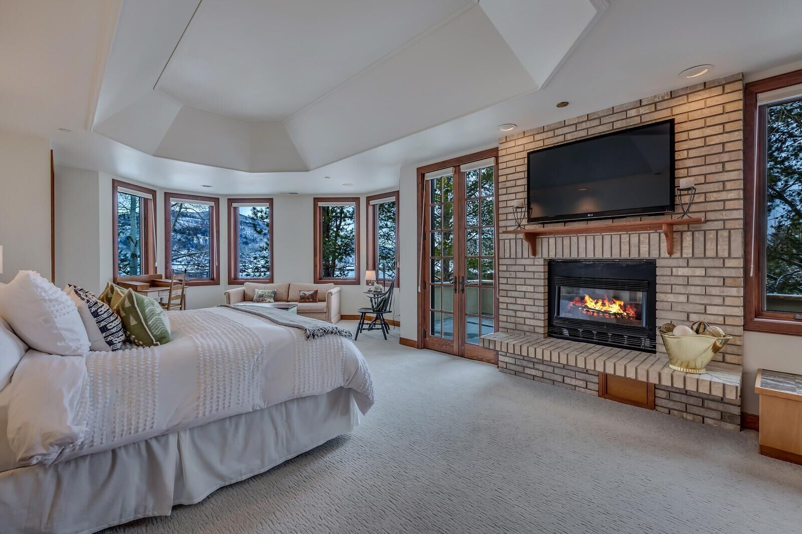 Un dormitorio amplio con una cama grande, una chimenea y un televisor instalado en la pared.