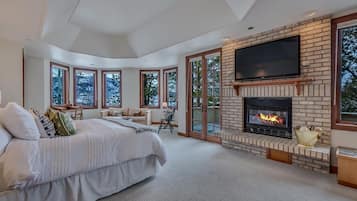 Un dormitorio amplio con una cama grande, una chimenea y un televisor instalado en la pared.