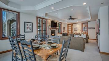 A dining area with a wooden table and chairs, a fireplace, and a sofa in the background.