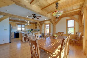 Une cuisine spacieuse avec des poutres apparentes, un coin repas doté d’une grande table en bois et un ventilateur de plafond.