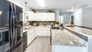 A modern kitchen with white cabinets, a black refrigerator, a granite countertop, and a microwave. - Fire Pit & Dock: Lake of the Ozarks Retreat! (Roach)