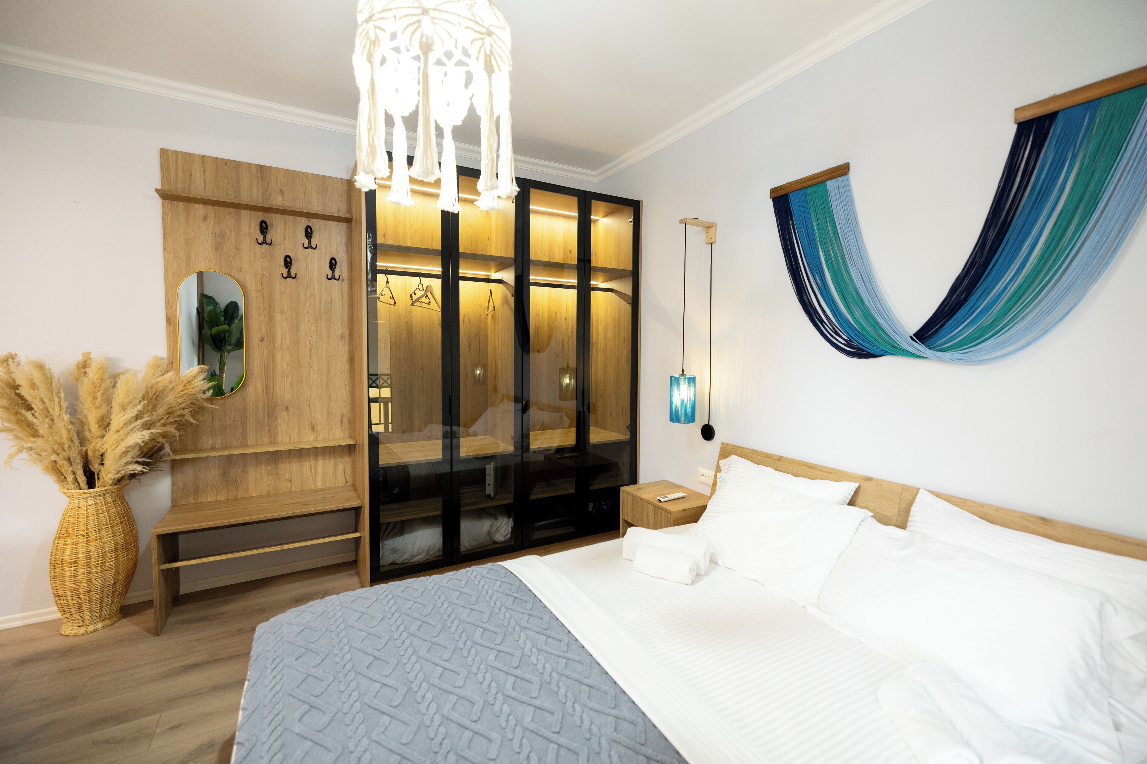 Un dormitorio moderno con una cama grande, un armario de madera, una hamaca colgante y una mesita de noche con lámpara.