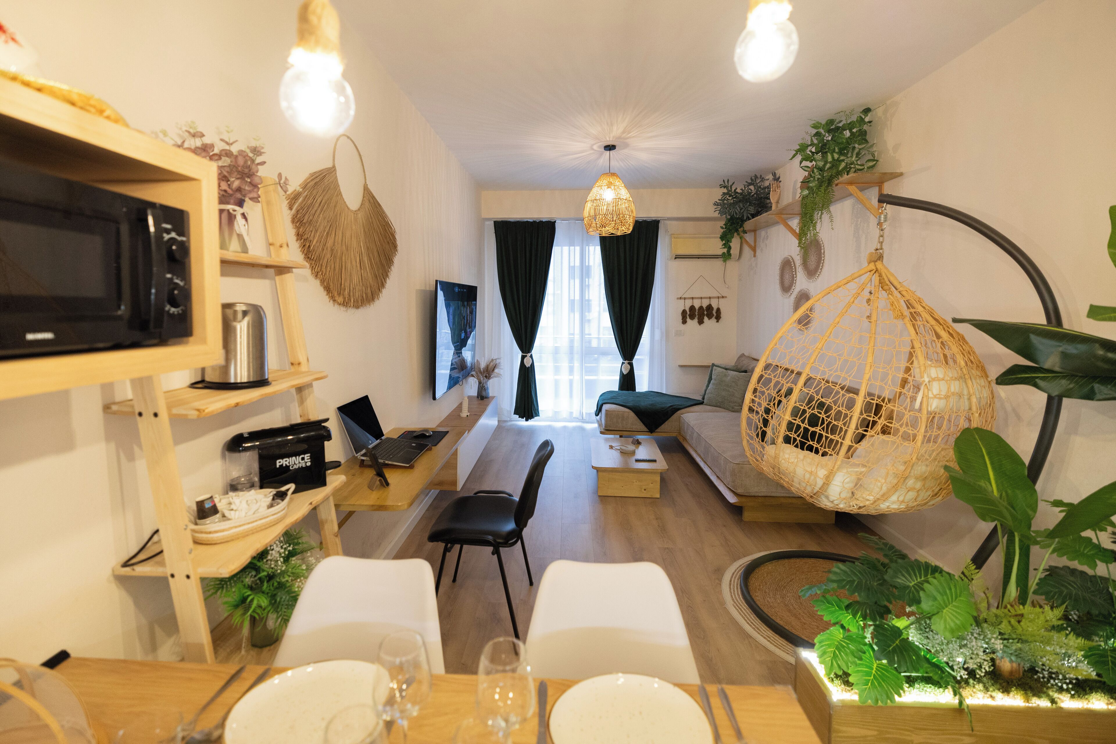 Een moderne woonkamer met een houten eettafel voor vier personen, een bank, een hangstoel en een televisie op een plank.