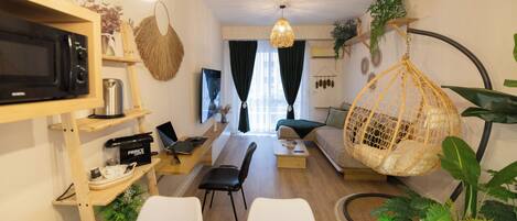 Una sala de estar moderna con una mesa de comedor de madera preparada para cuatro personas, un sofá, una silla colgante y un televisor en un estante.