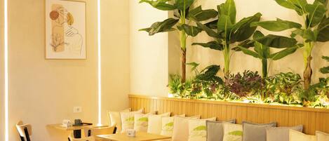 A restaurant with wooden tables and chairs, a wall-mounted light fixture, and a large potted plant.