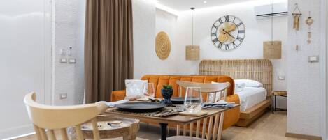 A modern, well-lit room with a dining table set for two, a sofa, and a bed with a headboard.