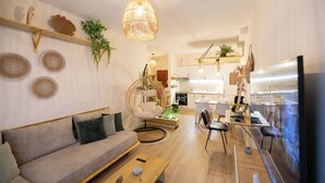 A modern living room with a sofa, coffee table, and hanging chair. There is a kitchen area in the background with cabinets and a dining table. -  Boho Central Apartment (Tirana)