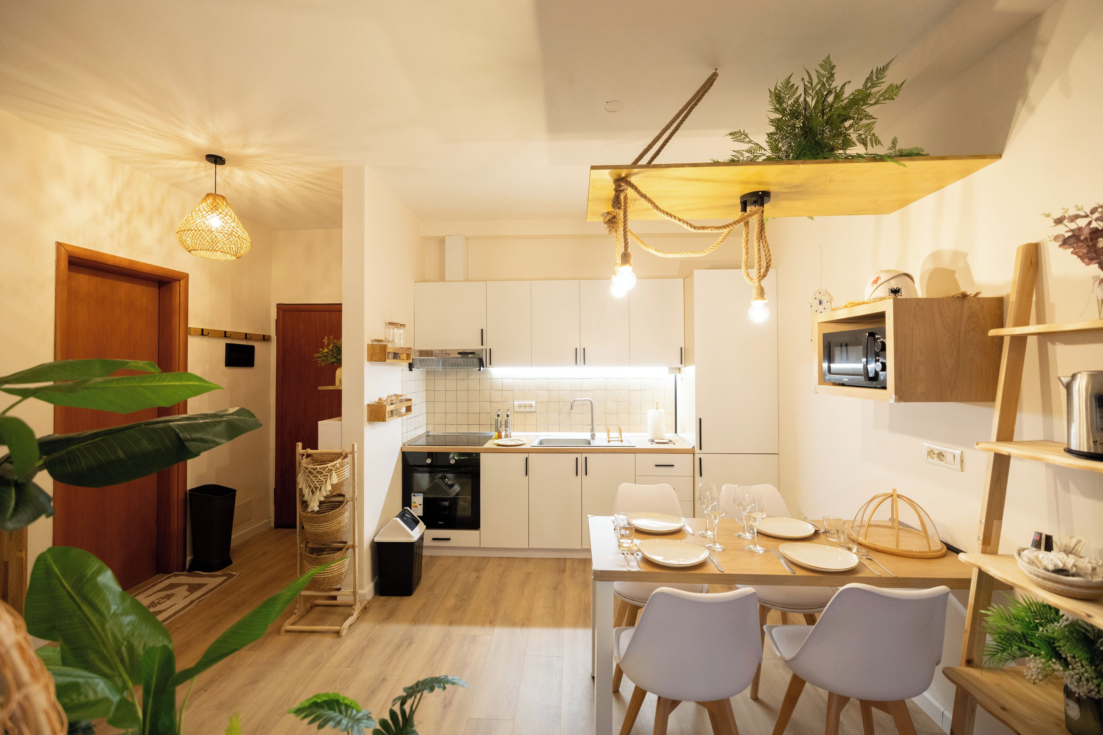 Une cuisine moderne avec des meubles blancs, une table à manger en bois et deux chaises blanches.
