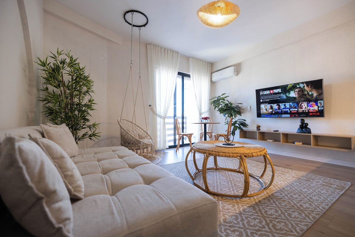 A living room with a sofa, a round table, a hanging light fixture, and a TV displaying a show.