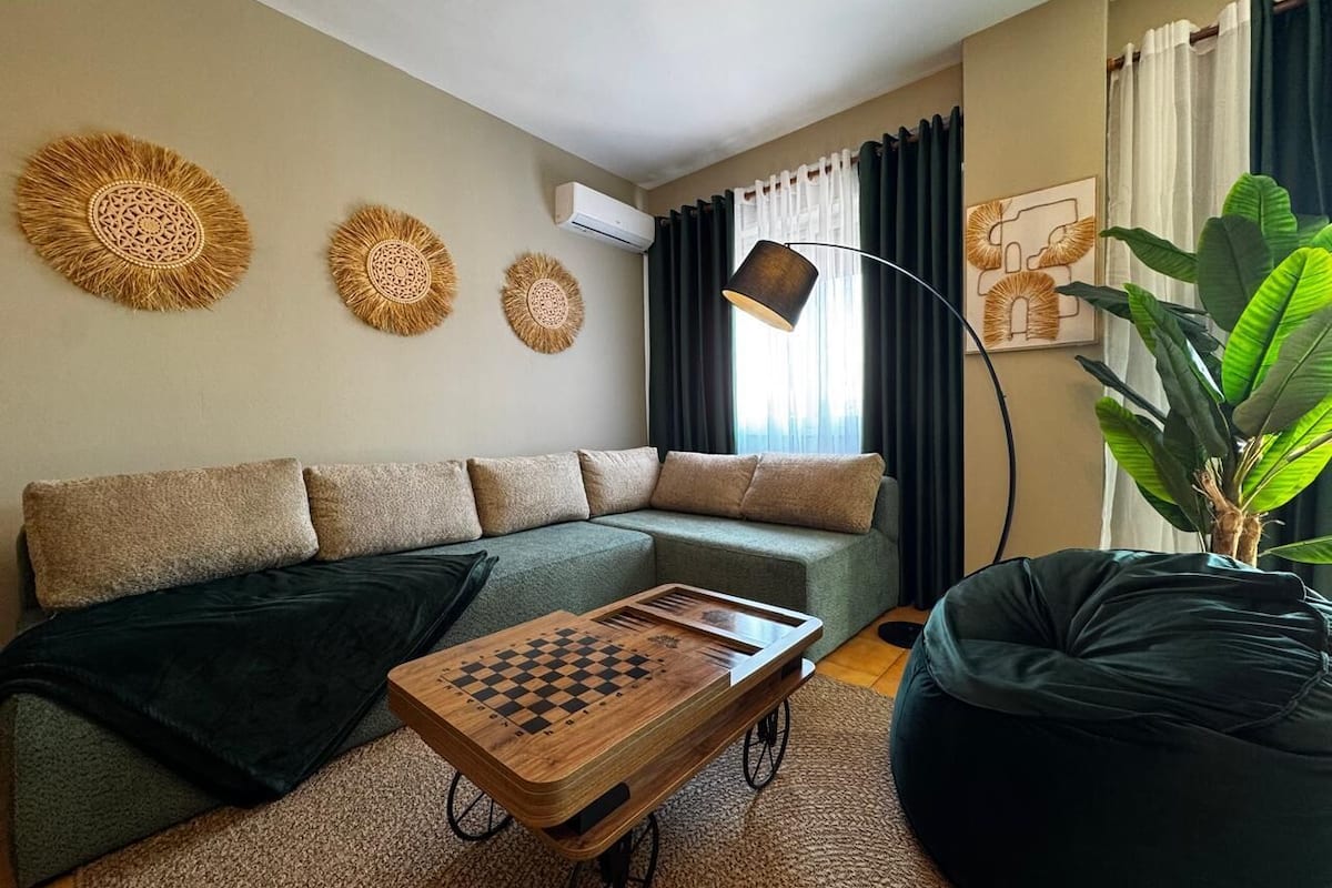 A living room with a sectional sofa, a wooden coffee table, a black bean bag, a floor lamp, and decorative wall art.