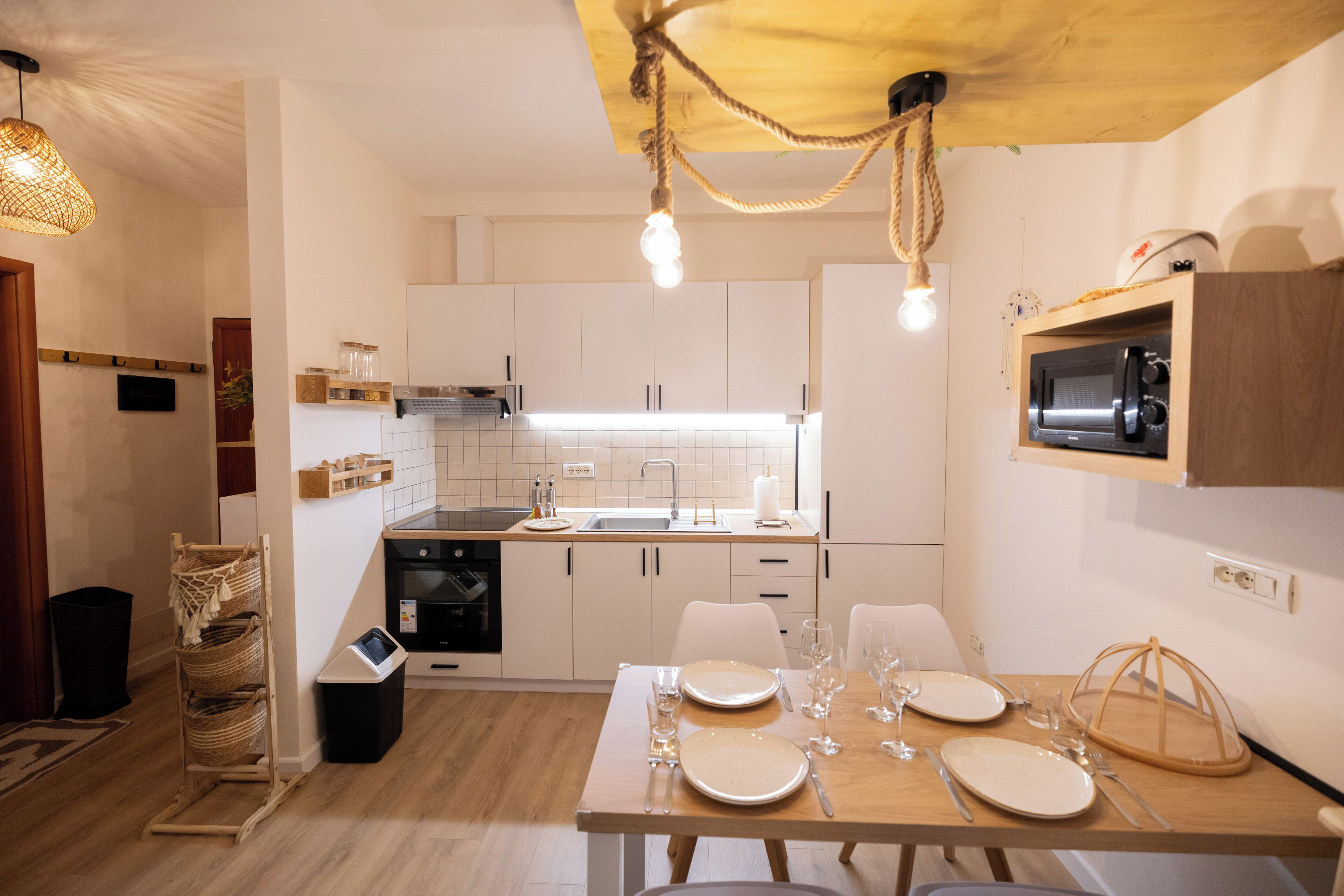 A modern kitchen with white cabinets, a wooden dining table set for four, and a microwave above it.